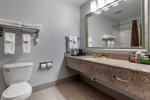 A bathroom with a toilet, sink, and mirror. There are towels hanging on a rack and a shower curtain.