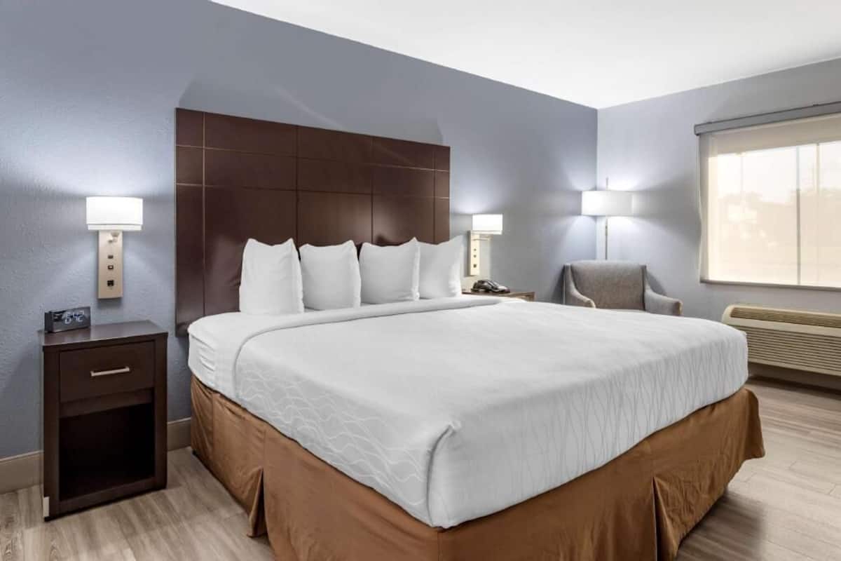 A hotel room with a large bed, bedside lamps, a chair, a nightstand, and a window.