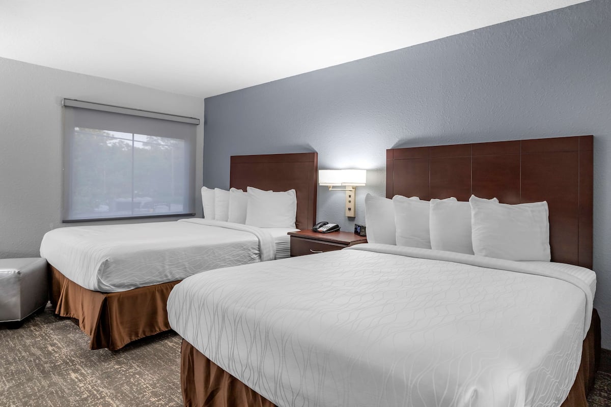 A hotel room with two beds, a window, a nightstand, and a lamp.