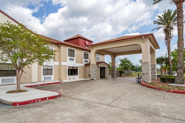 A hotel entrance with a covered walkway, a palm tree, and a clear sky.