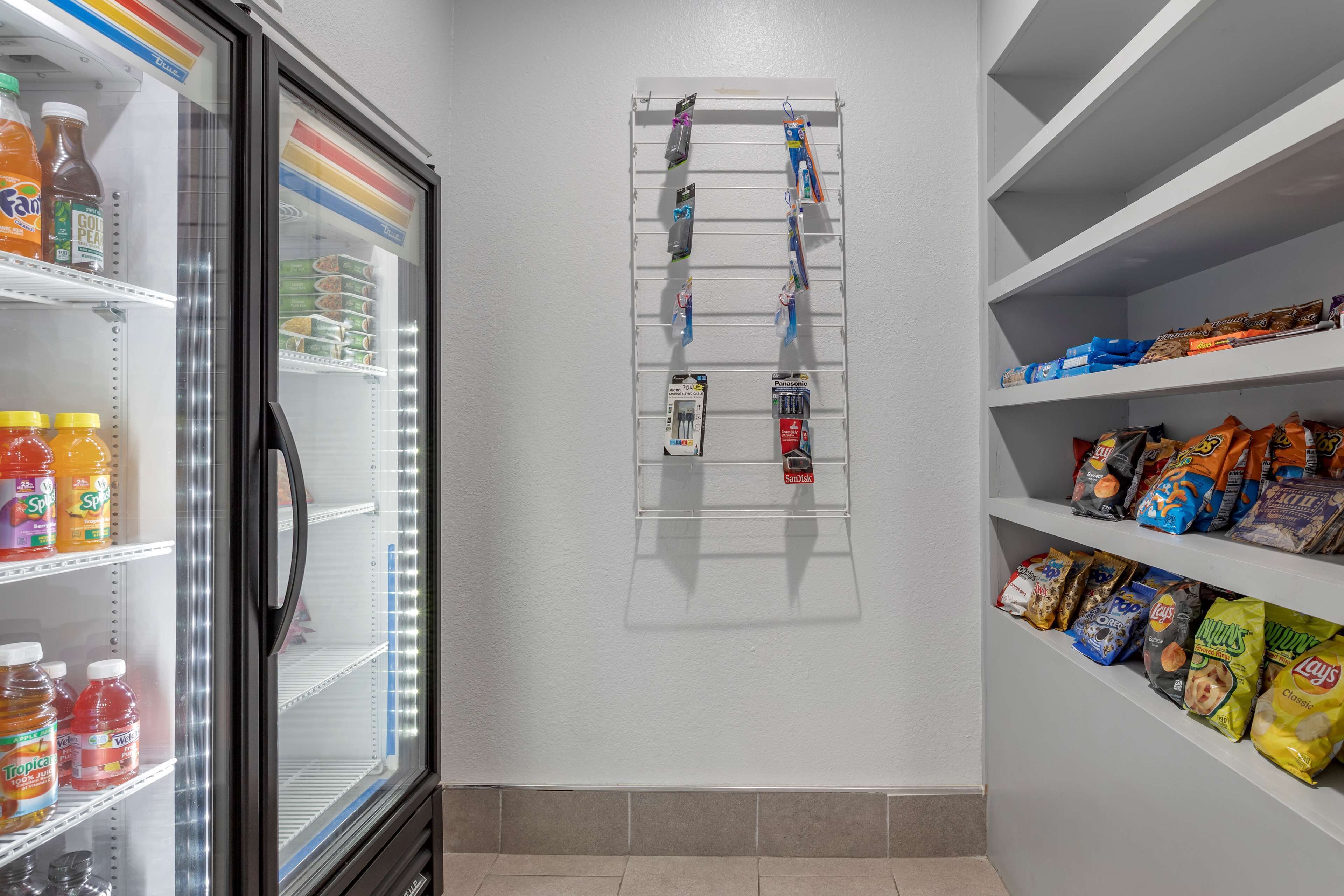 A storage area with shelves for snacks and beverages, a wall-mounted rack for hanging items, and a refrigerator with various drinks.