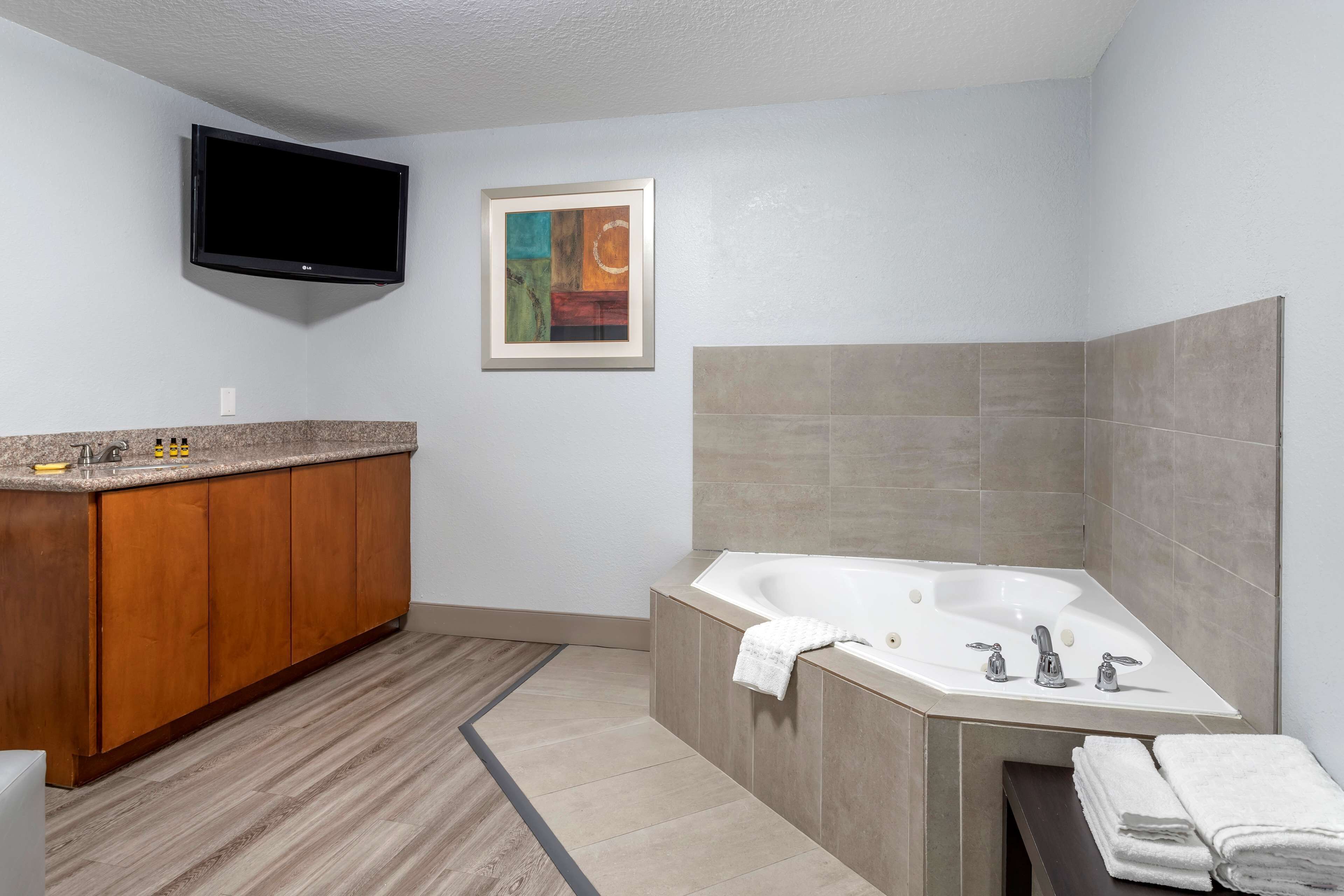 Un baño moderno con tocador de madera, una bañera grande y un televisor de pantalla plana montado en la pared.