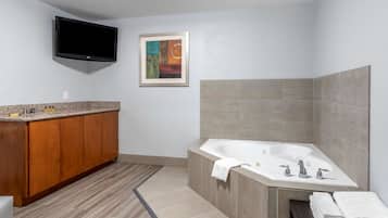 Un baño moderno con tocador de madera, una bañera grande y un televisor de pantalla plana montado en la pared.