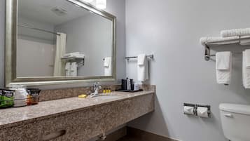 Et badeværelse med bordplade i granit, et stort spejl, et håndklædestativ, et toilet og en vask med sæbedispenser.