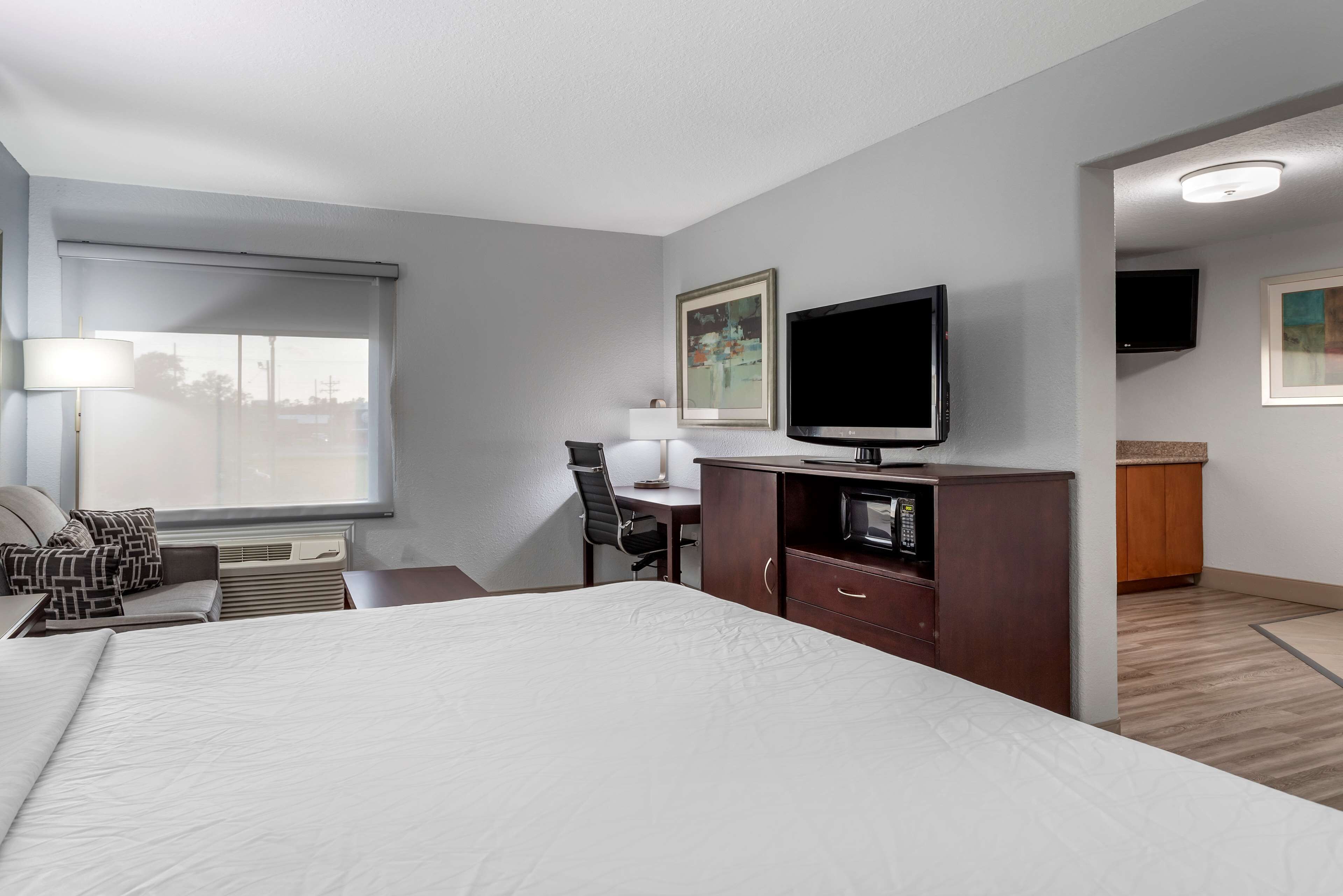 A hotel room with a large bed, a desk with a chair, a television, and artwork on the walls.