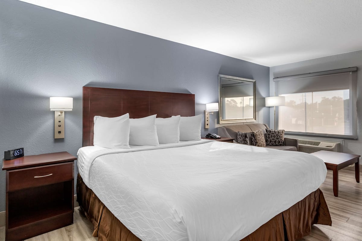 A hotel room with a large bed, bedside lamps, a nightstand, a window with a view, and a thermostat.