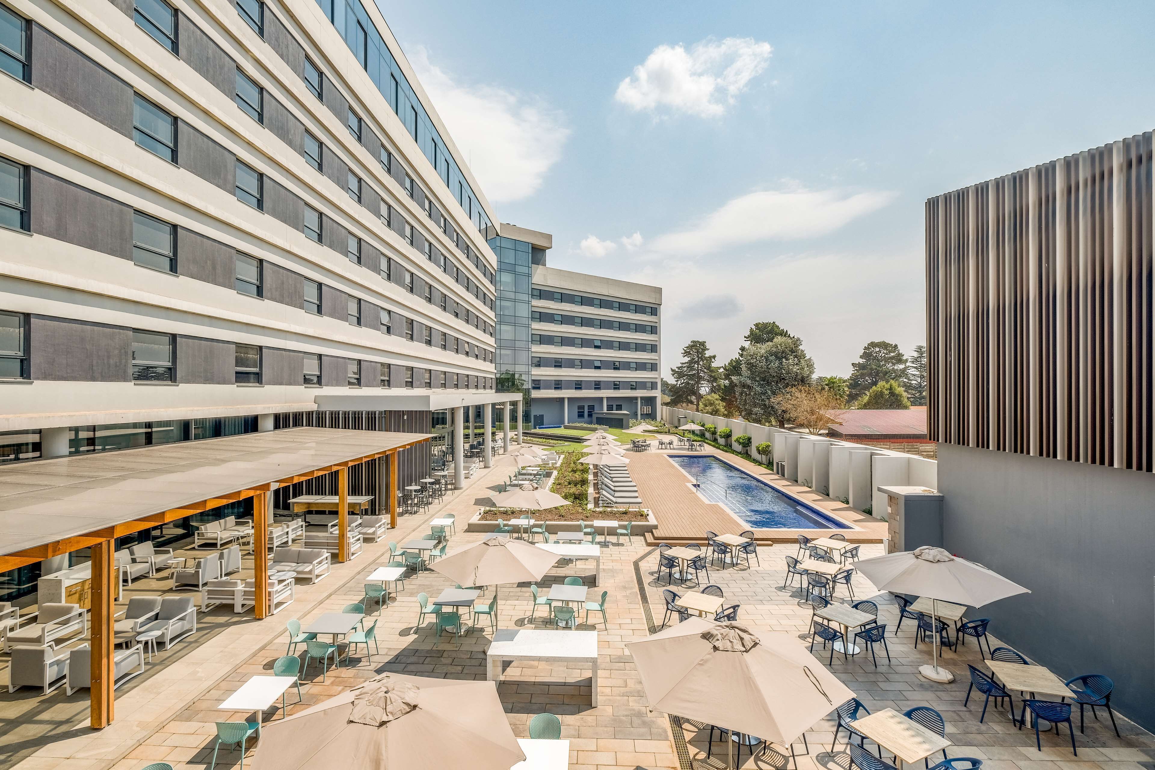A rooftop patio with outdoor seating, a swimming pool, and modern buildings in the background.