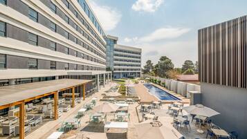 A rooftop patio with outdoor seating, a swimming pool, and modern buildings in the background.