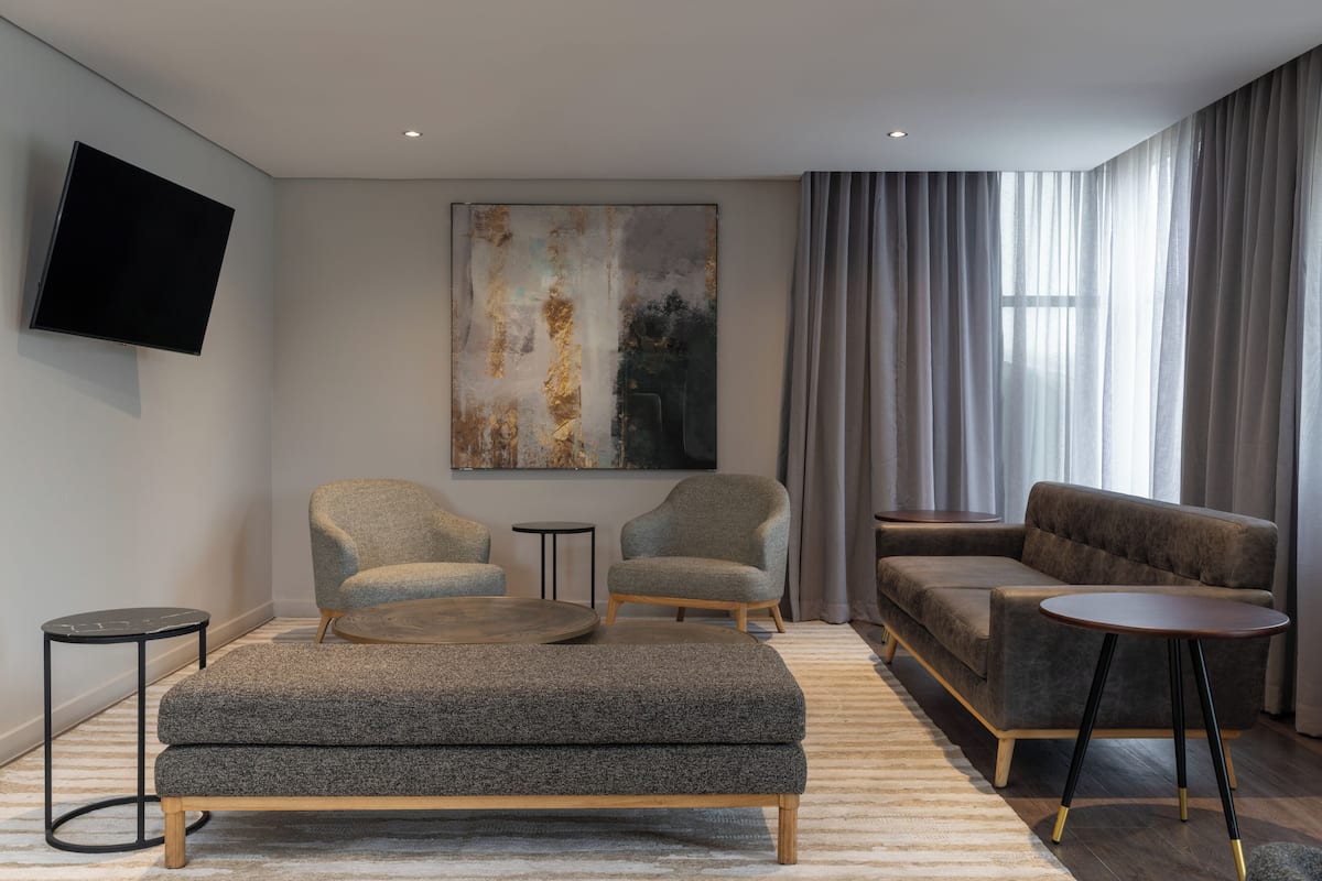 A modern living room with a sofa, two armchairs, a coffee table, a flat-screen TV, and a large abstract painting on the wall.