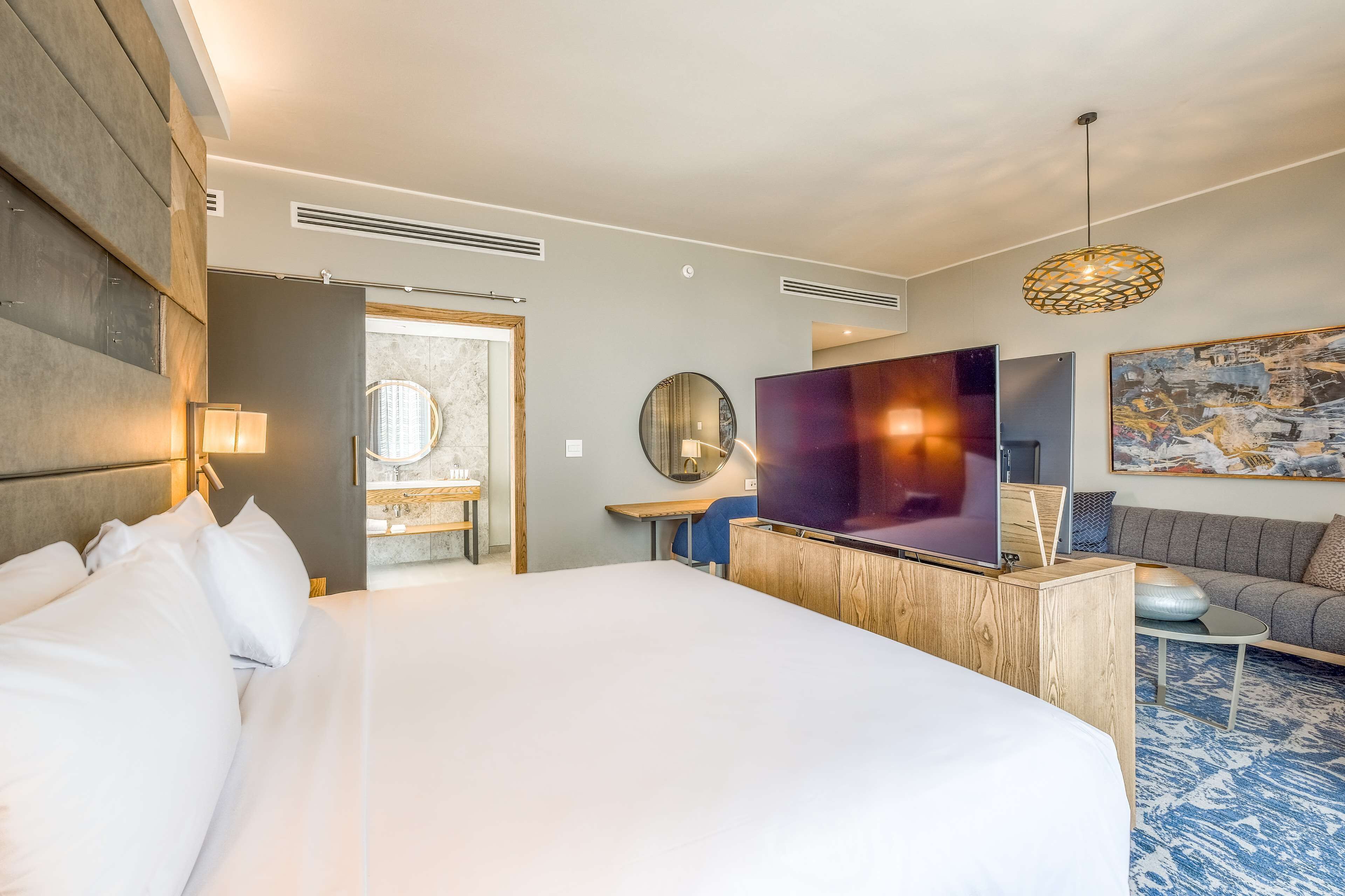A modern hotel room with a large bed, a TV, a sofa, and a desk.