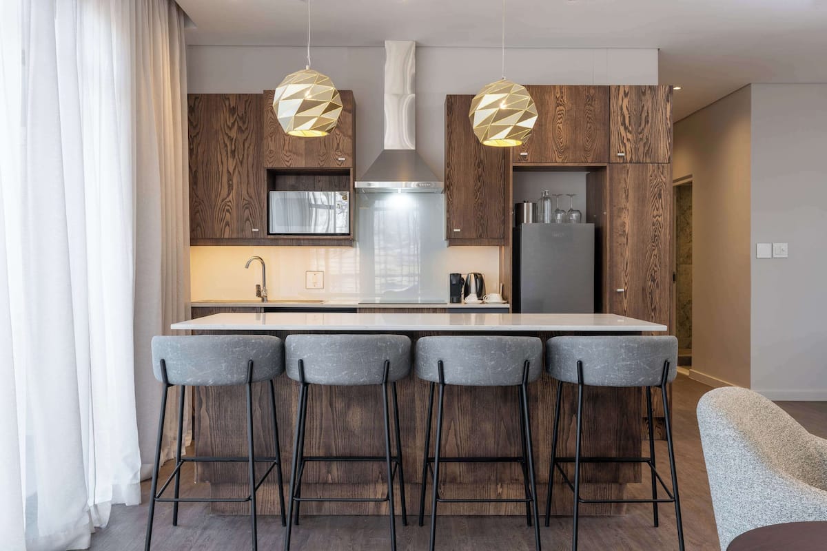 A modern kitchen with wooden cabinets, a central island with bar stools, stainless steel appliances, and pendant lighting.