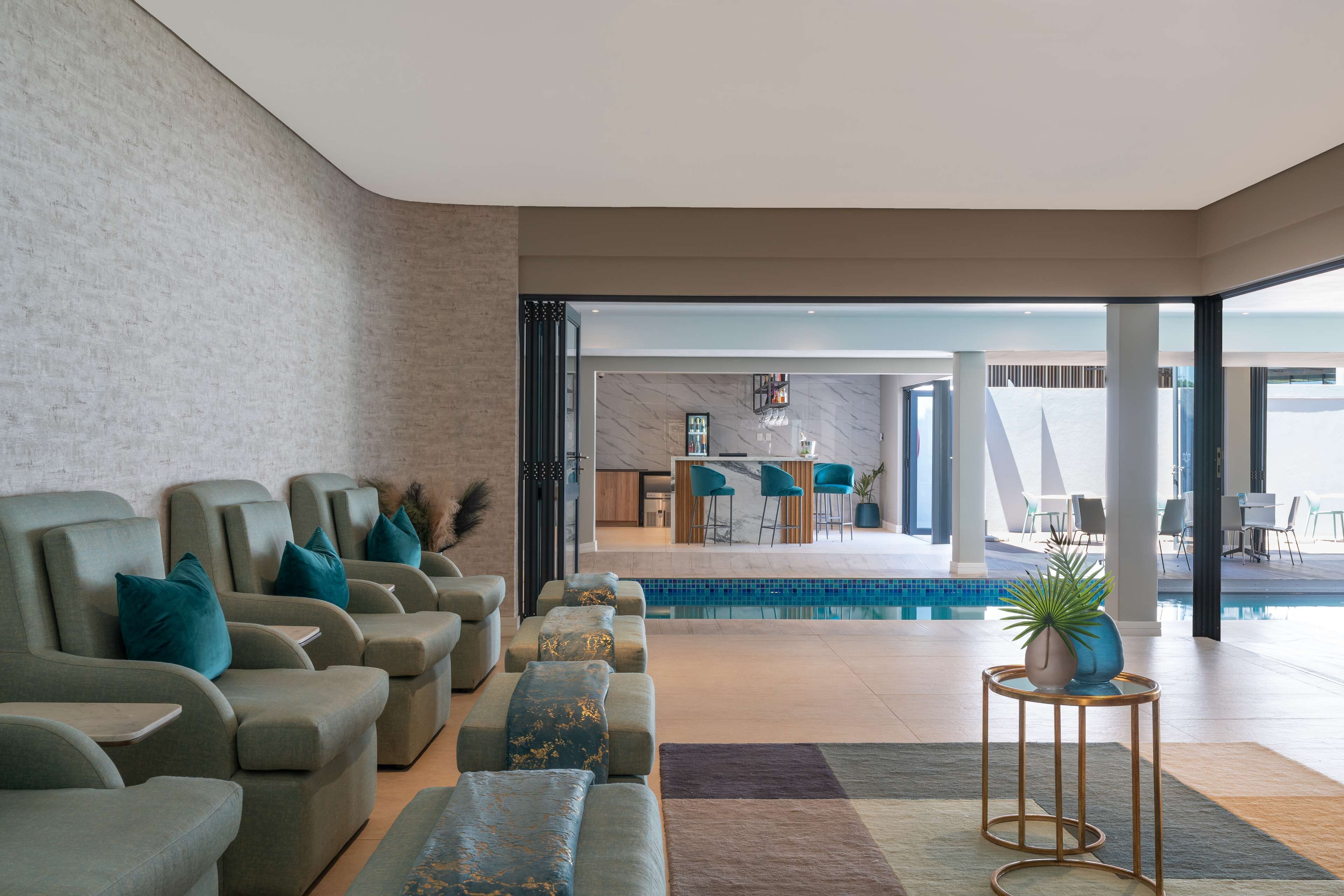 A modern lounge area with sofas and a small round table, a pool, and a bar area in the background.