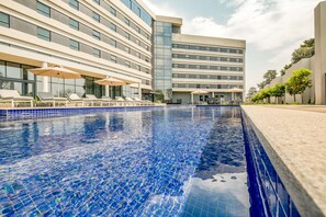 Un hotel moderno con piscina, tumbonas y un cielo azul despejado.