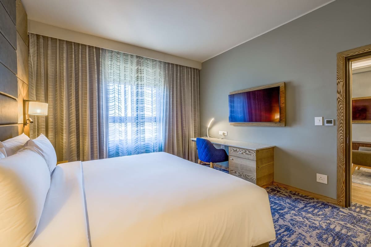 A hotel room with a large bed, a desk, a chair, a TV, and curtains.