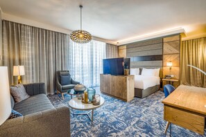 Habitación de hotel con cama, sofá, escritorio, silla, mesa auxiliar y televisión.