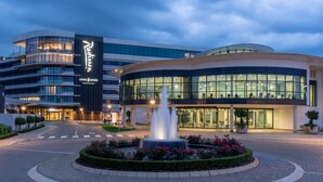 A modern hotel with a fountain in the courtyard, large glass windows, and a curved building facade. - Radisson Hotel and Convention Centre OR Tambo Airport (Kempton Park)