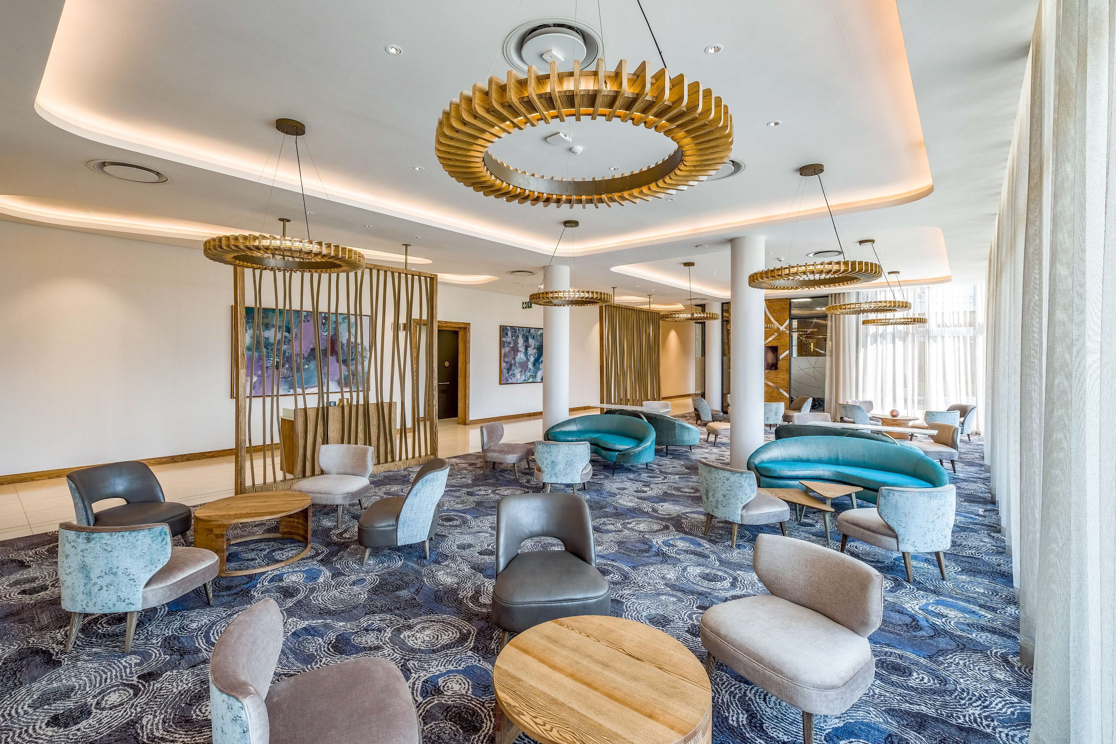 A spacious lobby with modern furniture, a patterned carpet, and unique ceiling lights.