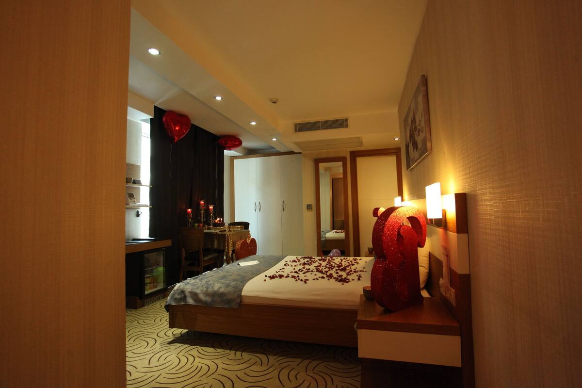 A hotel room with a bed, bedside table, and a large teddy bear decoration.