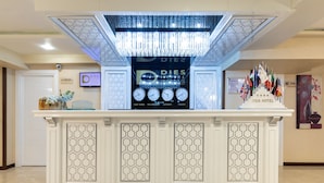 A reception desk with a chandelier, a clock displaying multiple time zones, and flags. - Dies Hotel (Diyarbakir)