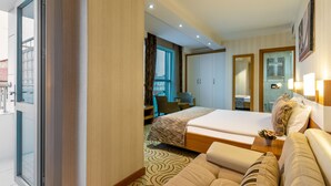 A modern hotel room with a large bed, a sofa, a desk, and a view of the city. - Dies Hotel (Diyarbakir)