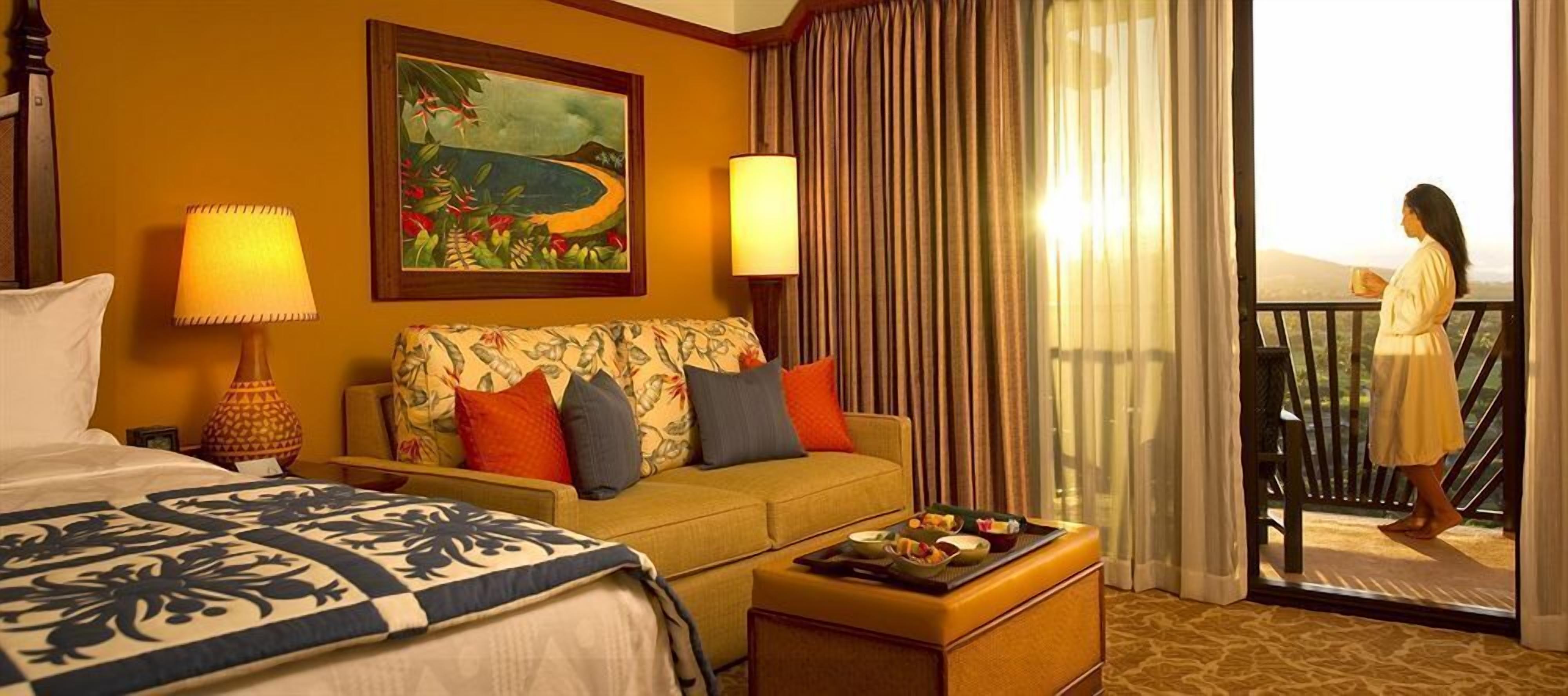 A hotel room with a bed, a sofa, a dining table with food, a painting on the wall, and a balcony with a view.
