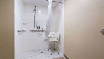 A shower area with a grab bar, a white chair, and a towel rack.