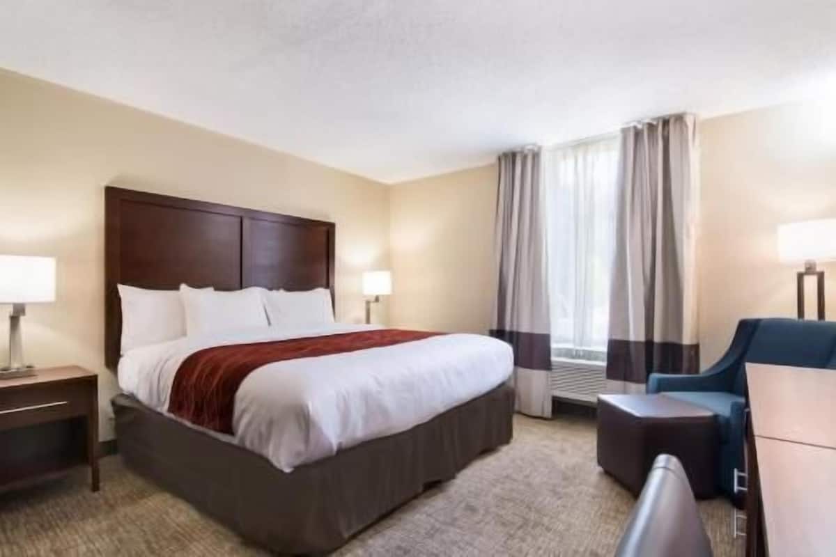 A hotel room with a large bed, bedside tables, a desk, a chair, and a window with curtains.