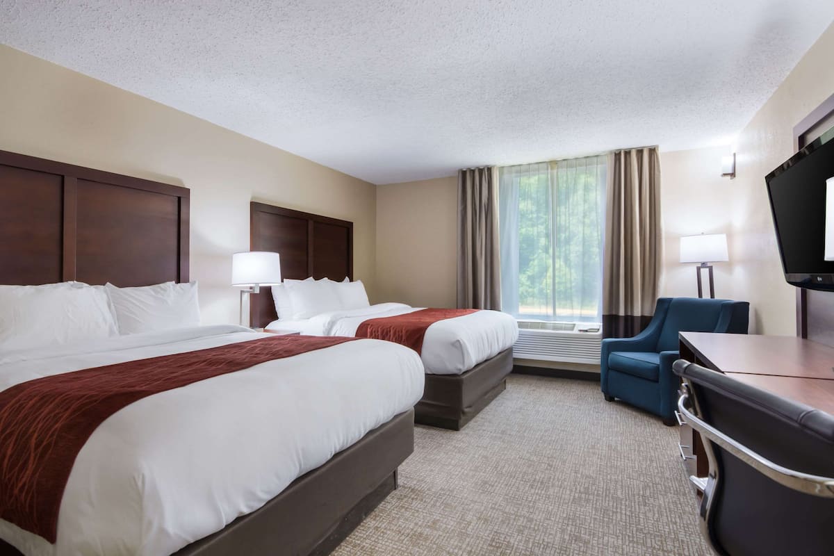 A hotel room with two beds, a desk, a chair, a TV, and a window with curtains.