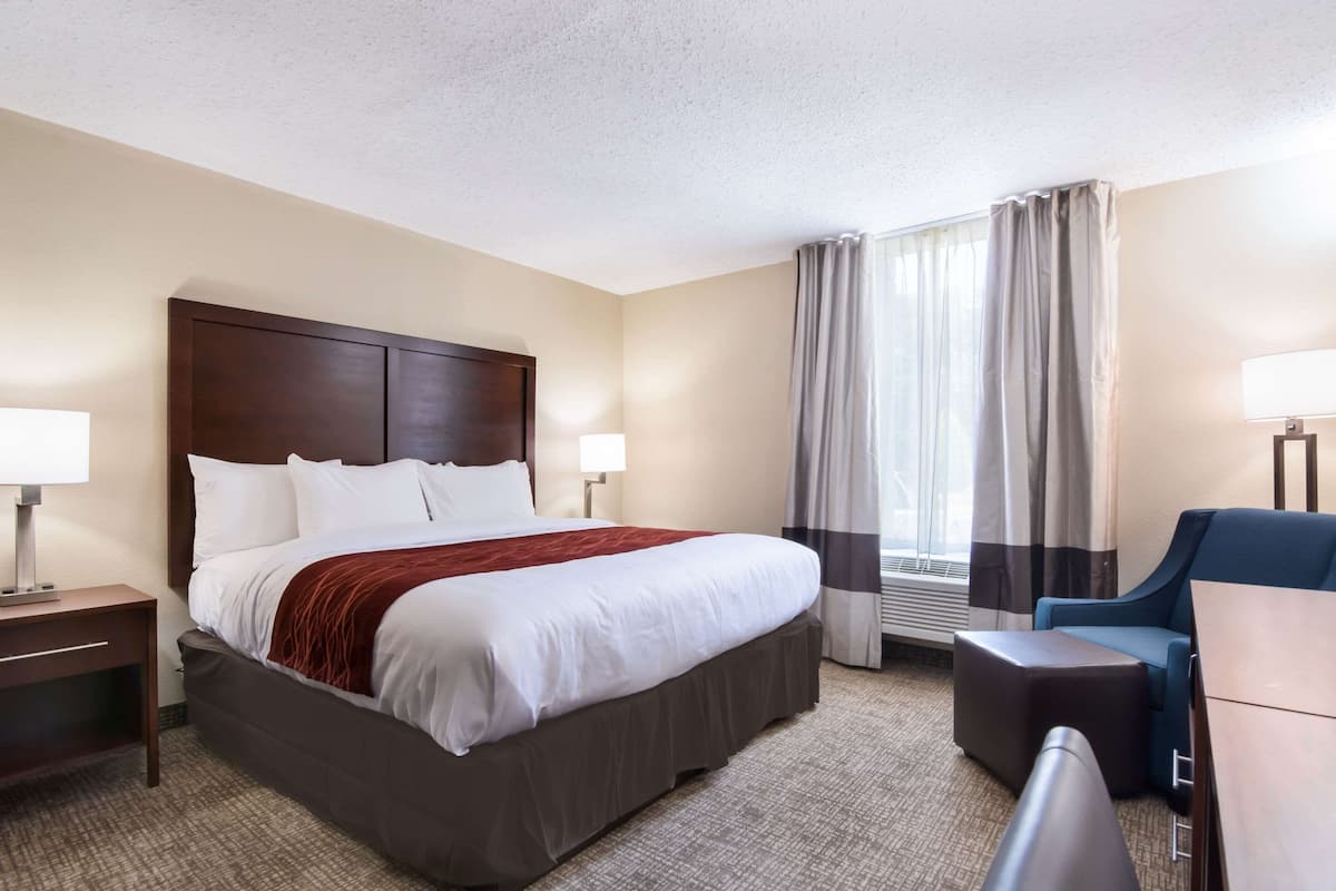 A hotel room with a large bed, a desk, a chair, and a window with curtains.