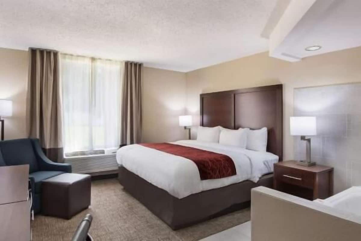 A hotel room with a large bed, two bedside tables with lamps, a desk, a chair, and a window with curtains.