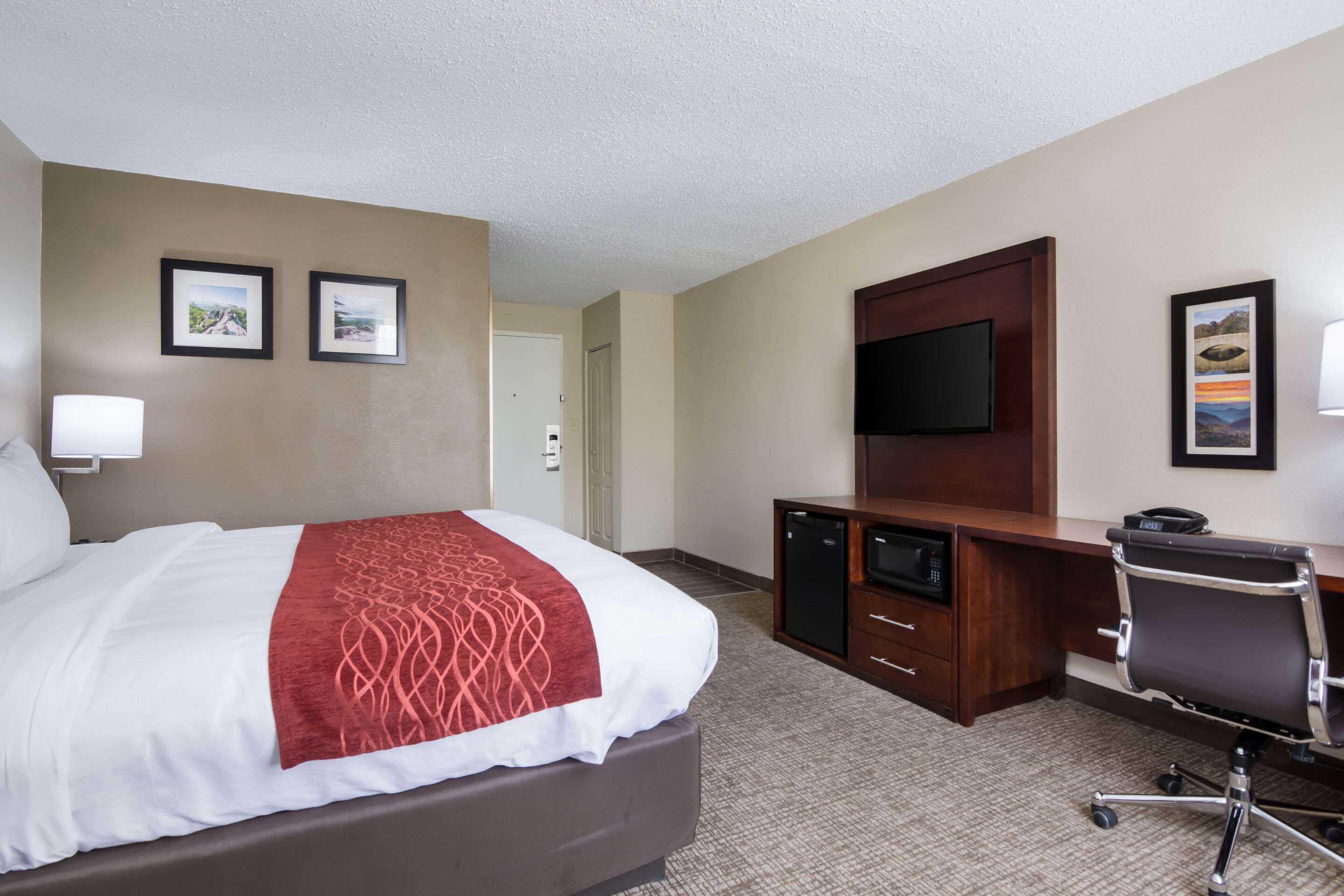 Ein Hotelzimmer mit einem Bett, einem Schreibtisch, einem Sessel, einem Fernseher und zwei gerahmten Bildern an der Wand.