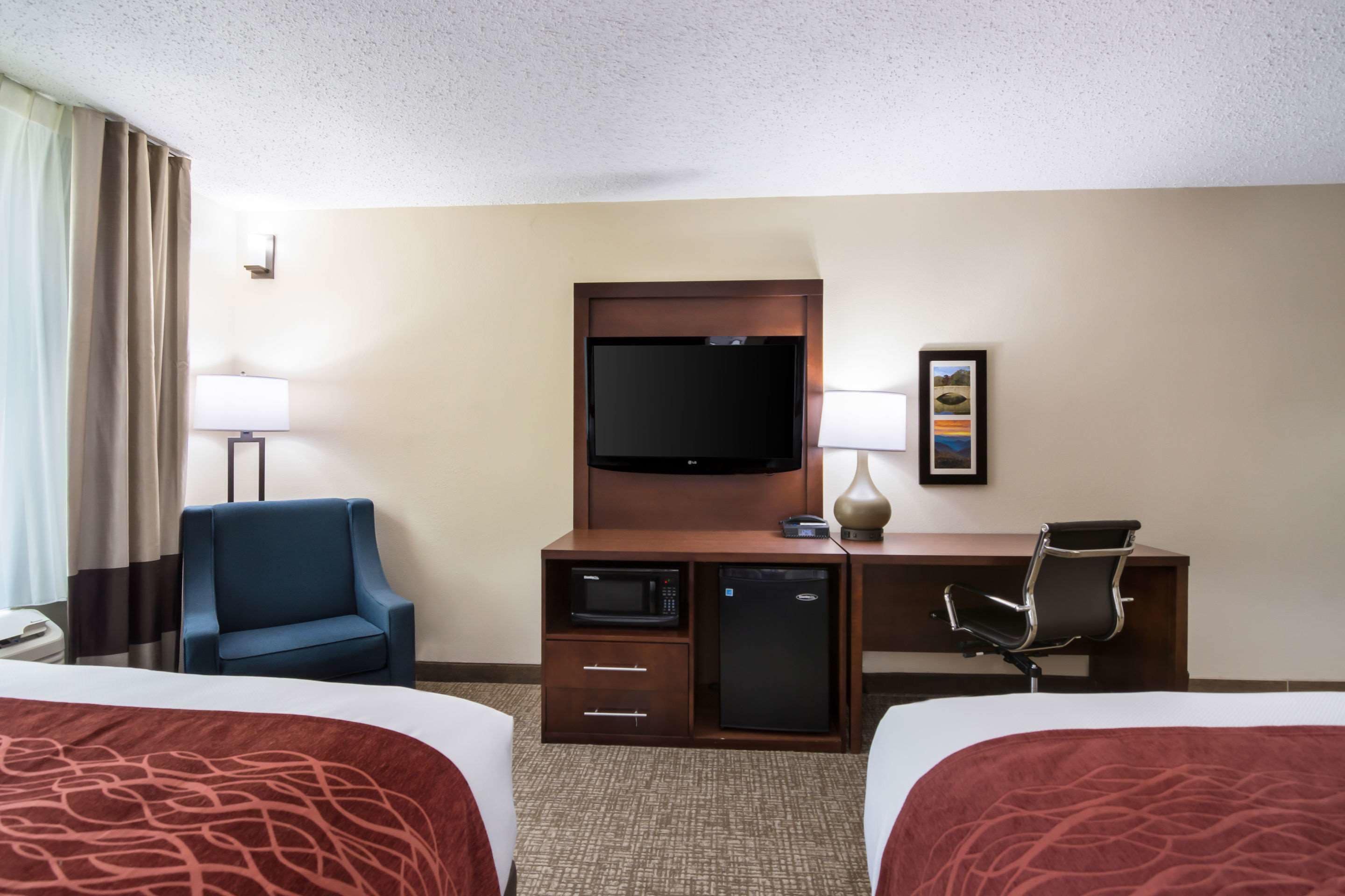 Una habitación de hotel con dos camas, un escritorio, televisión, microondas y refrigerador.