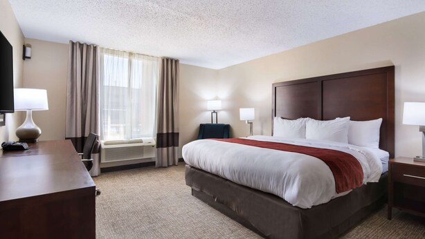 A hotel room with a large bed, a desk, a chair, a TV, a lamp, and a window with curtains. - Comfort Inn Kings Mountain (Kings Mountain)