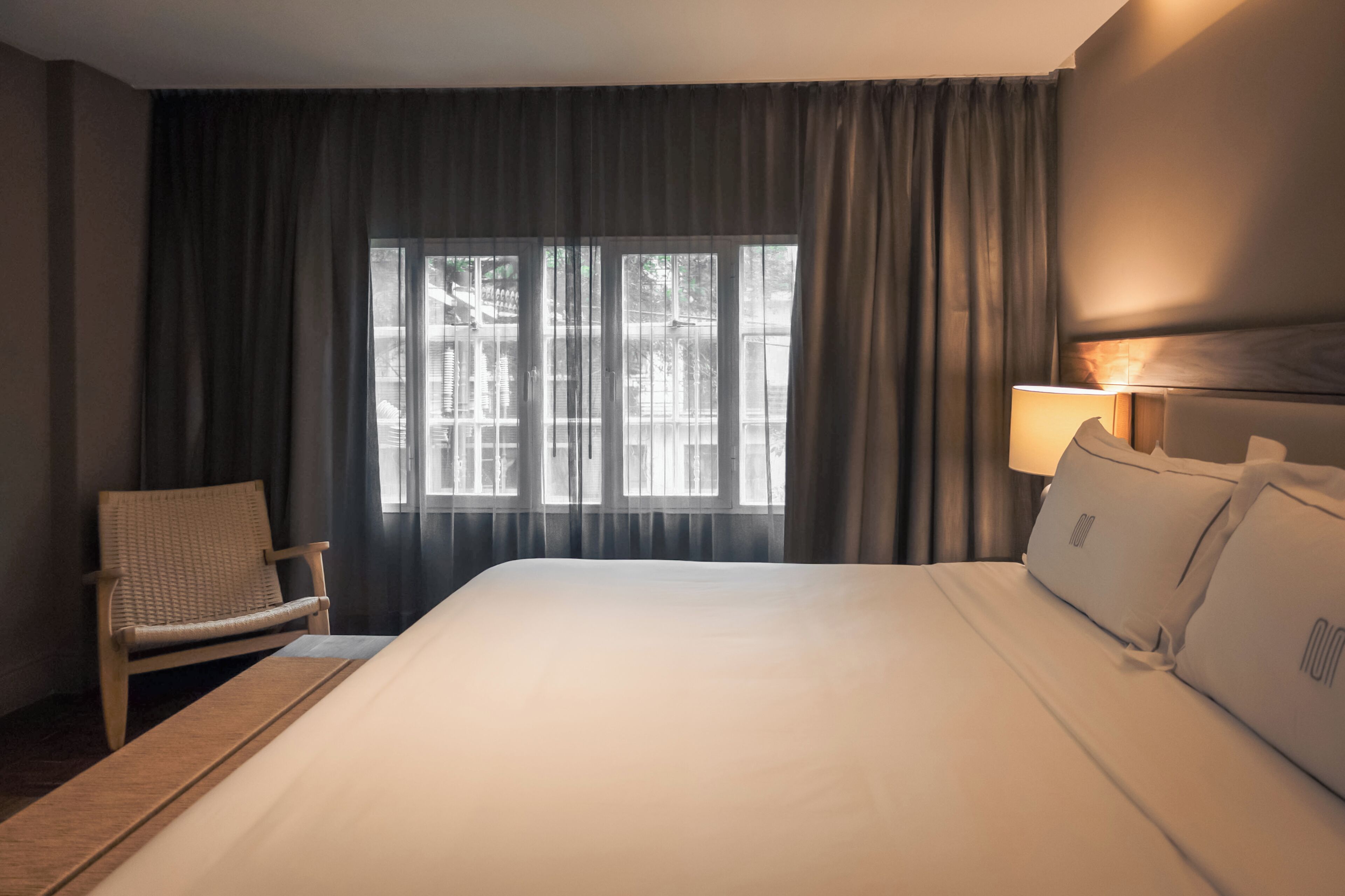 Ein Hotelzimmer mit einem großen Bett, einem Sessel, einer Lampe und einem Fenster mit Vorhängen.