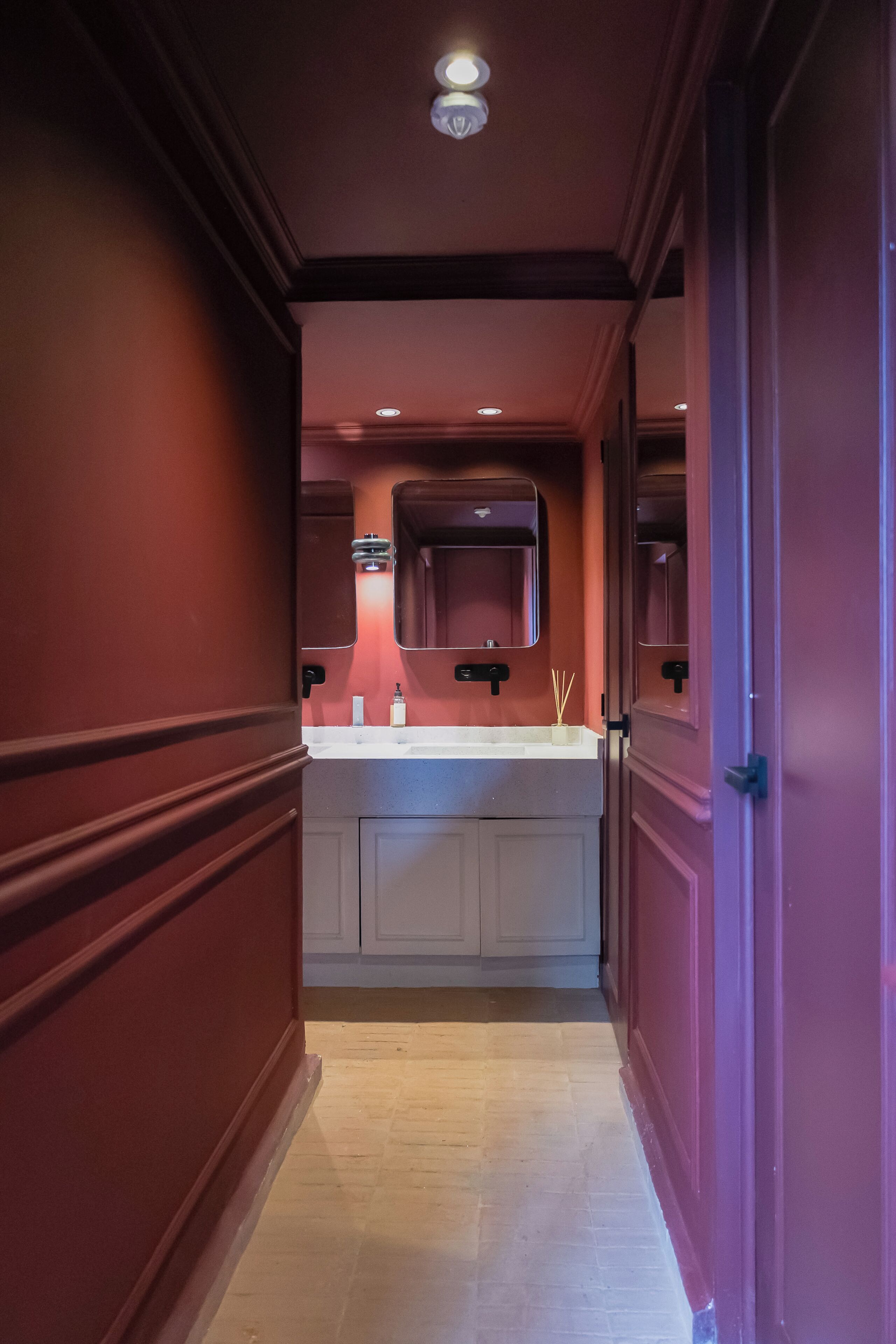 A hallway leading to a bathroom with a sink, mirror, and recessed lighting.