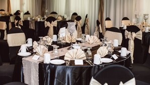 En festlokal med runda bord uppdukade för ett formellt evenemang, där varje bord har placeringskort, glas och elegant bordsdekoration.