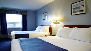 Ett hotellrum med två sängar, ett nattduksbord, en lampa och en inramad tavla på väggen.
