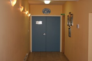 Un pasillo con una puerta azul identificada como 'Atlantic Room', luminarias en la pared y un letrero verde que indica el camino a las escaleras.