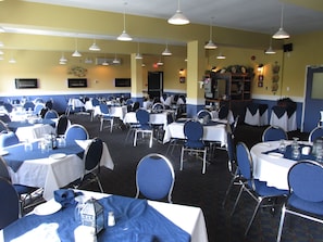 Un salón de banquetes con varias mesas dispuestas para comer, sillas e iluminación colgante.
