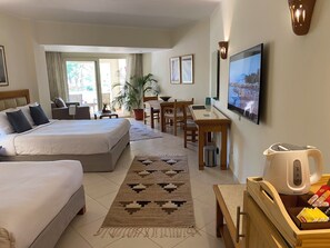 A hotel room with a bed, a desk, a chair, a potted plant, and a television.