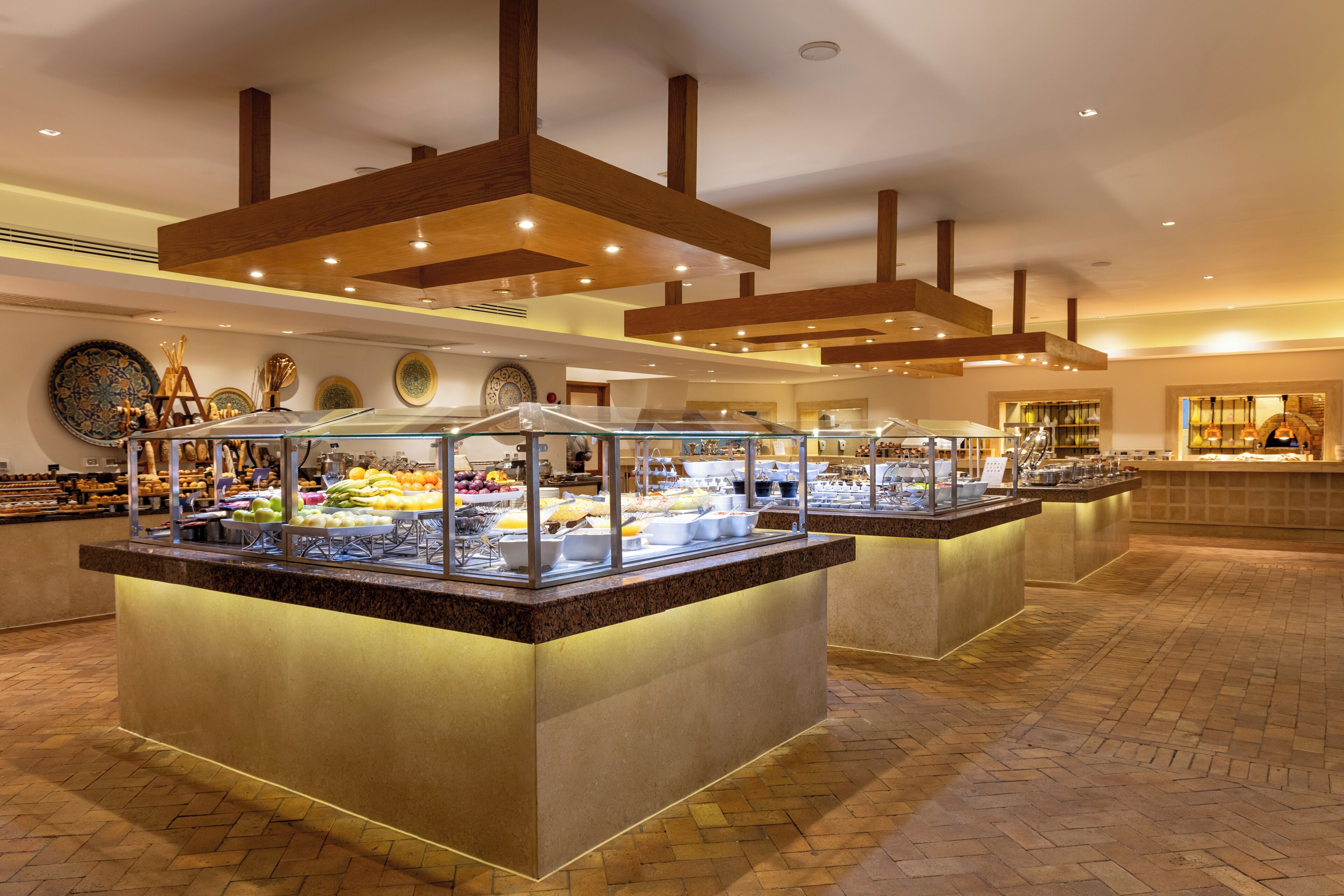 Un espace buffet doté de plusieurs présentoirs de nourriture, d’un sol à motifs et d’un plafond avec des poutres en bois et des luminaires encastrés.