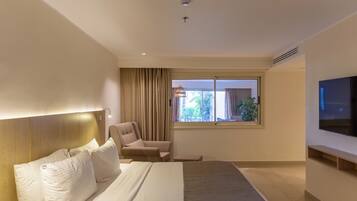 Una habitación de hotel moderna con cama, sillón, televisor y ventana con cortinas.