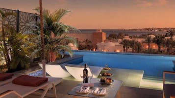 Un área de comedor junto a la piscina con vista al mar y una estructura que recuerda a un castillo al fondo.