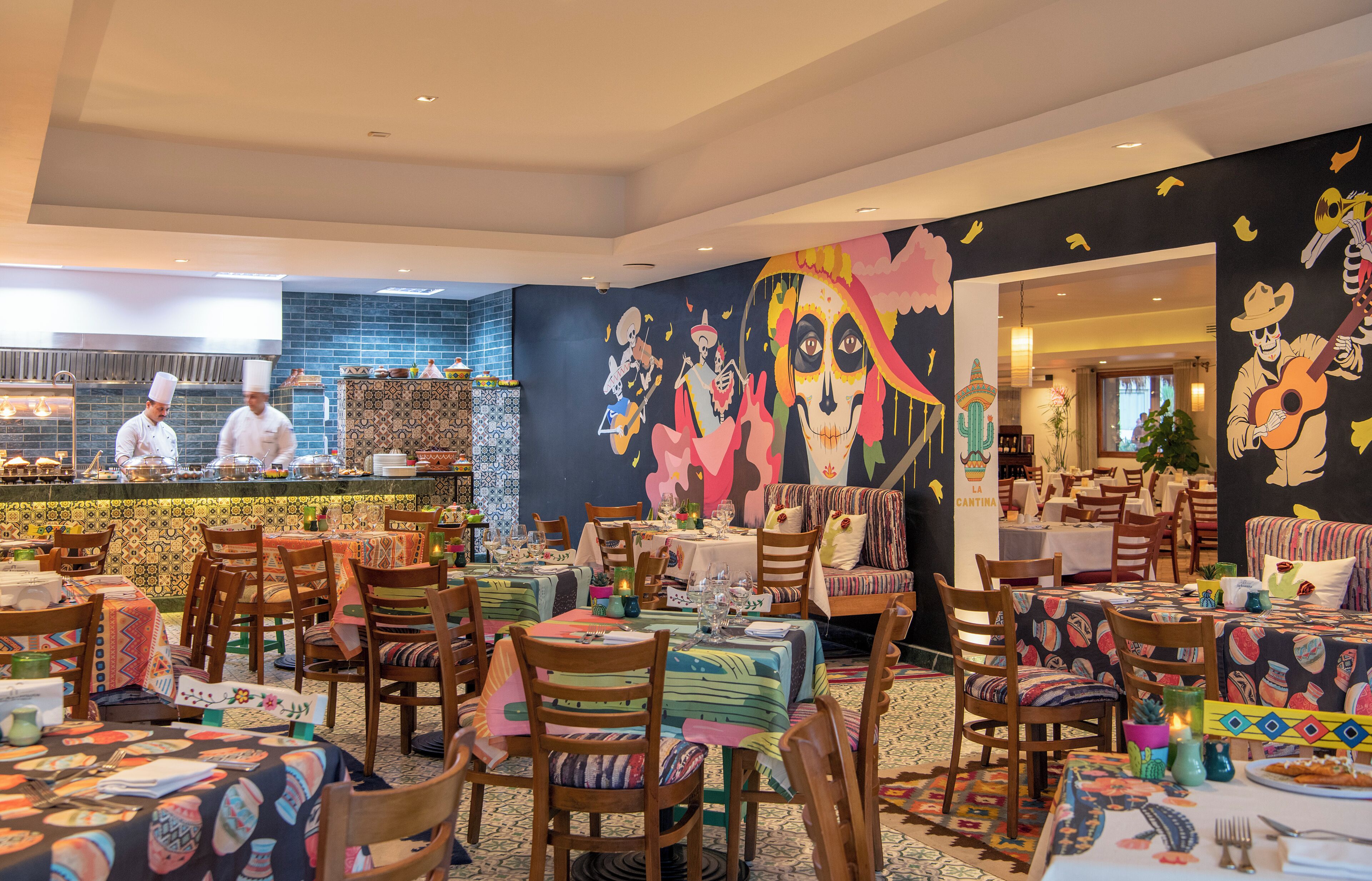 A restaurant with a vibrant mural, multiple dining tables, and a kitchen area with chefs.