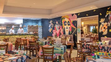 A restaurant with a vibrant mural, multiple dining tables, and a kitchen area with chefs.