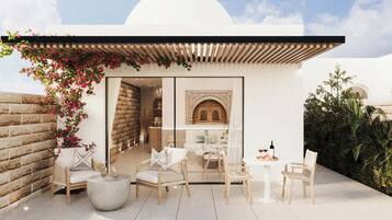 Un espace extérieur moderne aménagé avec des sièges, un mur blanc, une pergola en bois et une vue sur une pièce dotée d’une arche d’époque.