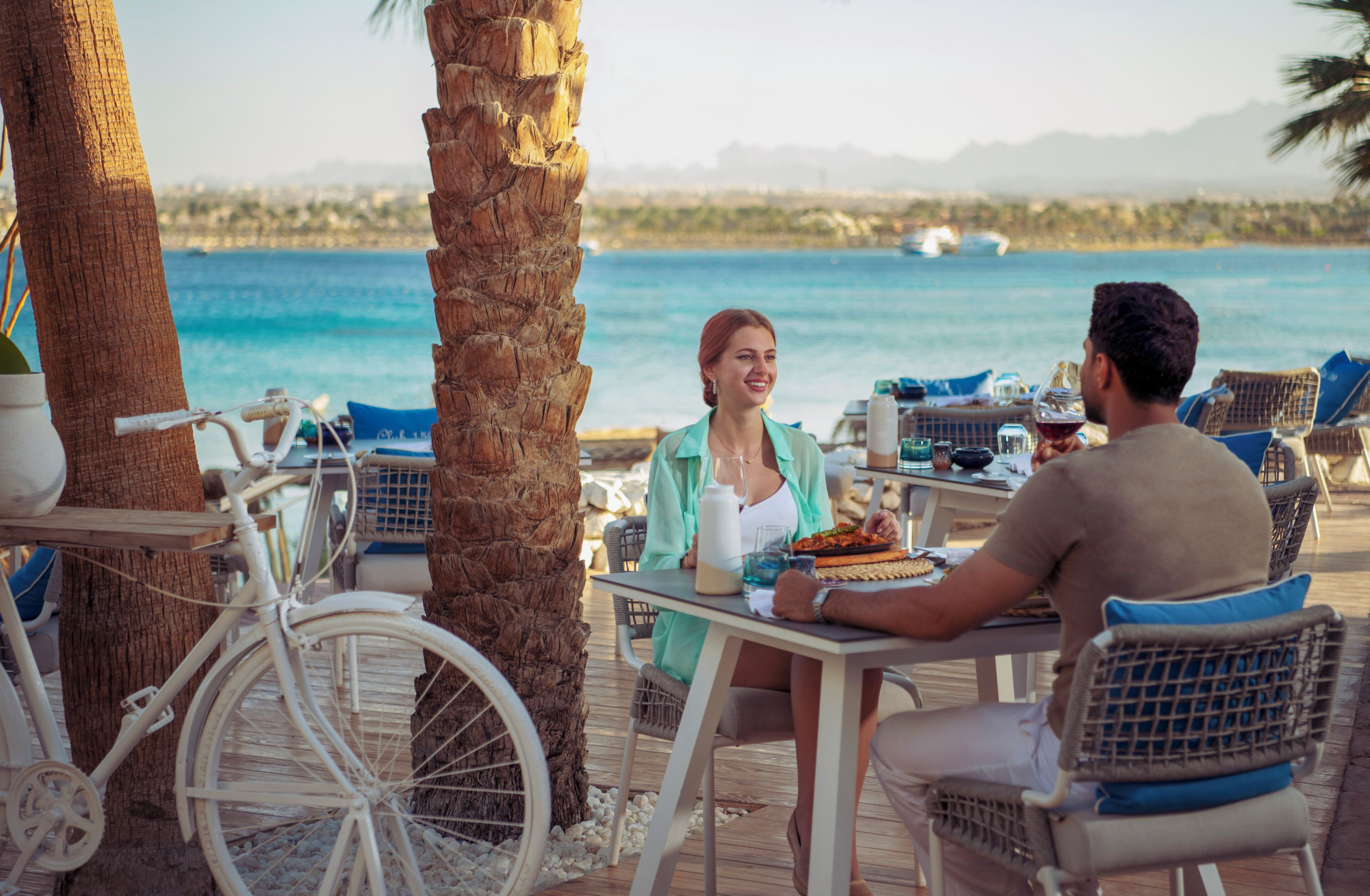 Una pareja cenando en una mesa al aire libre con vistas al mar y montañas.