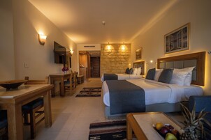 Quarto de hotel com cama, escrivaninha, cadeira, televisão e parede de pedra.