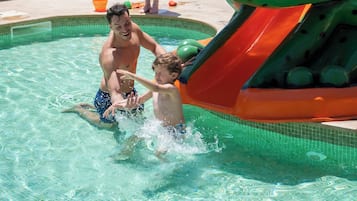 A swimming pool with a slide shaped like a frog, lounge chairs, and palm trees in the background.