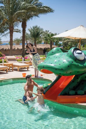 A swimming pool with a slide shaped like a frog, lounge chairs, and palm trees in the background.